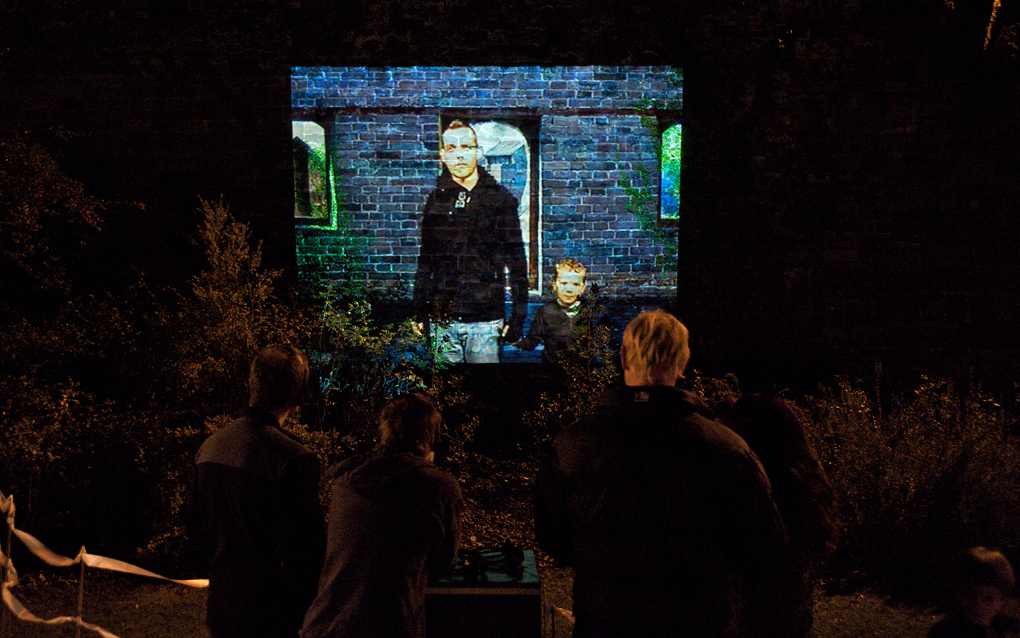 A large scale outdoor projection onto a Roman Wall of performer Andrew Westerside, holding his 3 year old son's hand.while stood on the great wall of China. (Through the Walls).
