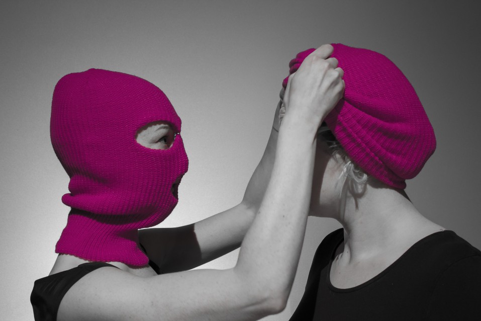 Main promo image for Proto-type Theater's 'A Machine they're Secretly Building'. Two women wearing hot pink balaclavas facing each other. It's not clear whether the balaclavas are being put on or taken off.